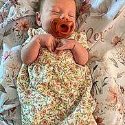 Remi is registered to the contest to win money with this photo: baby, pacifier, floral_dress, sleeping, blanket, flower_pattern, infant, hands, cozy, cute, peaceful, resting, indoors, soft, young_child, portrait, child, skin, head, comfort
