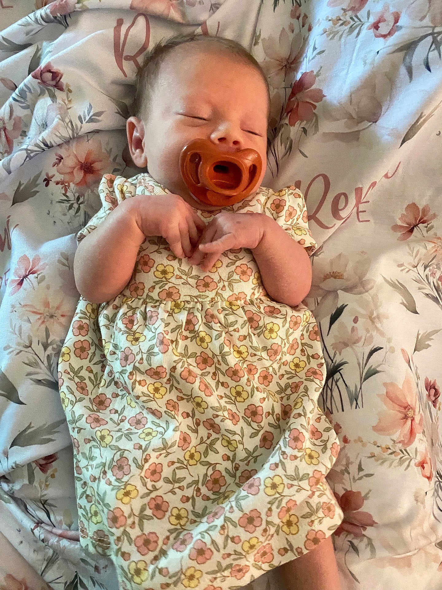 Remi is registered to the contest to win money with this photo: baby, pacifier, floral_dress, sleeping, blanket, flower_pattern, infant, hands, cozy, cute, peaceful, resting, indoors, soft, young_child, portrait, child, skin, head, comfort