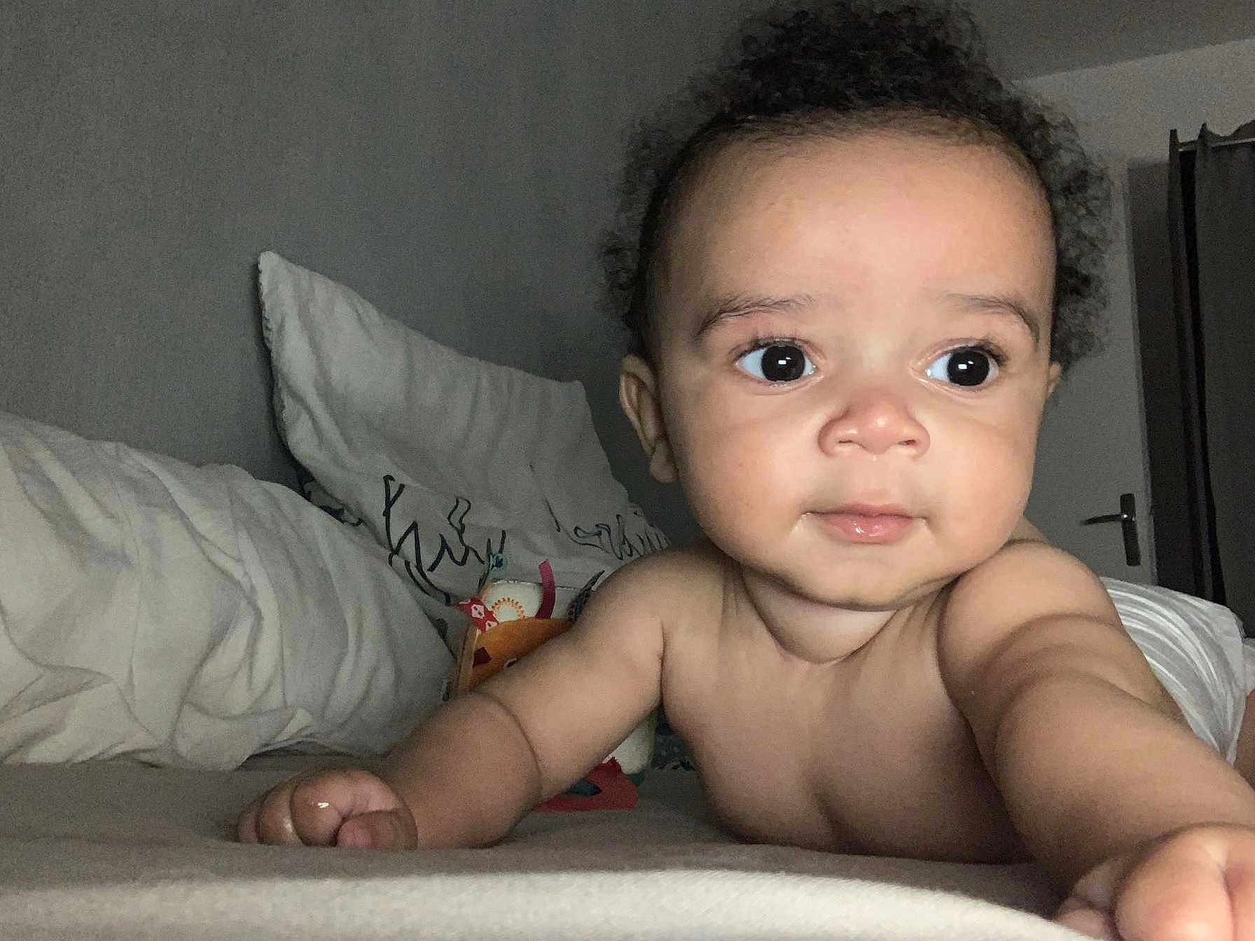 Keylan participe au concours pour gagner de l'argent avec cette photo : baby, child, infant, bed, pillow, arm, hand, face, skin, eyes, curly_hair, expression, indoor, room, blanket, door, reaching, closeup, person, lying_down