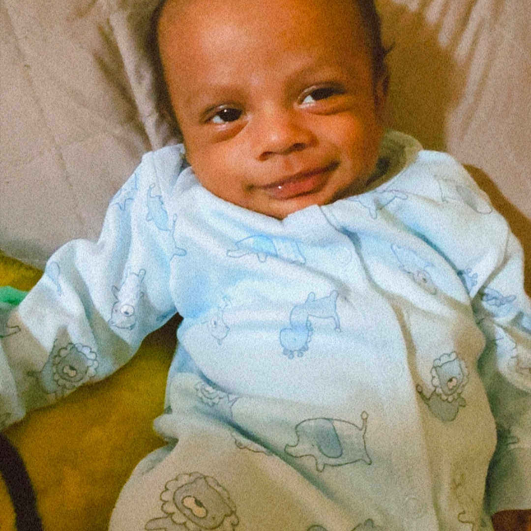 Samuel joined the competition — help win amazing prizes! baby, infant, child, smiling, portrait, lying_down, bed, blanket, pajamas, animal_print, clothing, face, eyes, head, indoors, bedroom, cozy, happy, photograph, close_up