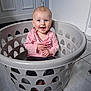 Leia is registered to the contest to win money with this photo: baby, child, laundry_basket, pink_clothing, smiling, happy, indoor, floor_tiles, sitting, cute, blue_eyes, short_hair, hands, toothy_grin, person, home, door, white_wall, casual, playful