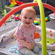 Leia is registered to the contest to win money with this photo: baby, child, play_gym, toy_balls, smiling, indoor, floor_mat, colorful, pink_shirt, leggings, happy, playtime, infant, cute, young_child, developmental_toys, childhood, fun, home, bright