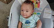 Ocean is registered to the contest to win money with this photo: baby, infant, baby_rocker, mittens, blue_clothing, car_print, indoor, carpet, wooden_furniture, cute, child, seated, colorful, toy_design, smiling, face, person, comfortable, home, curious