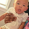 baby, infant, child, hand, adult_hand, white_shirt, striped_mitten, window, daylight, indoor, person, curious_expression, colorful_clothing, holding, seated, skin, face, shorts, casual_wear, cozy