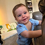 Oliver joined the competition — help win amazing prizes! baby, child, blue_onesie, smiling, indoor, living_room, couch, carpet, playmat, animal_patterns, cute, happy, young_child, person, portrait, home, furniture, infant, face, toddler