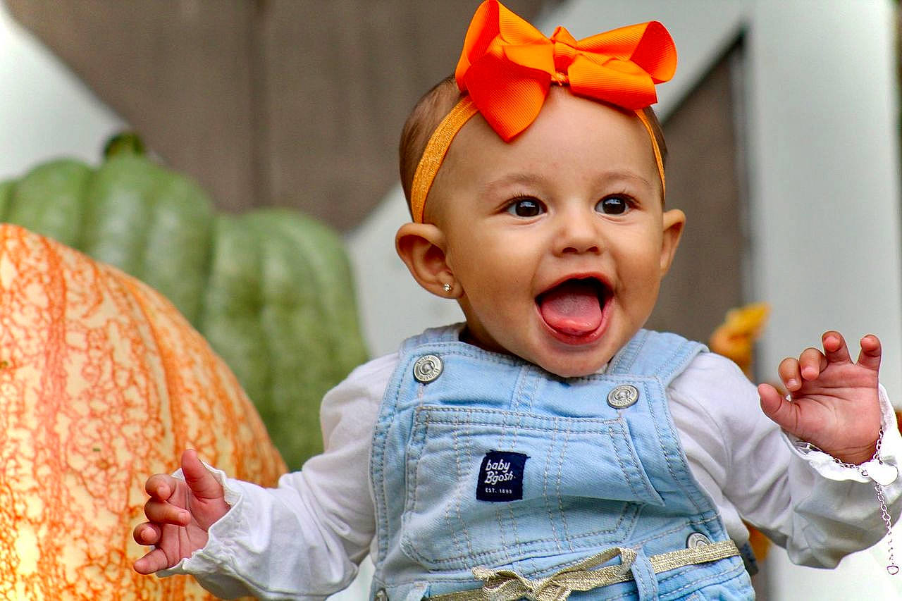 Elizah is registered to the contest to win money with this photo: baby, baby_toddler_clothing, cheek, child, eye, face, facial_expression, finger, fun, gesture, happy, human_body, nose, orange, organ, people, person, skin, sleeve, smile