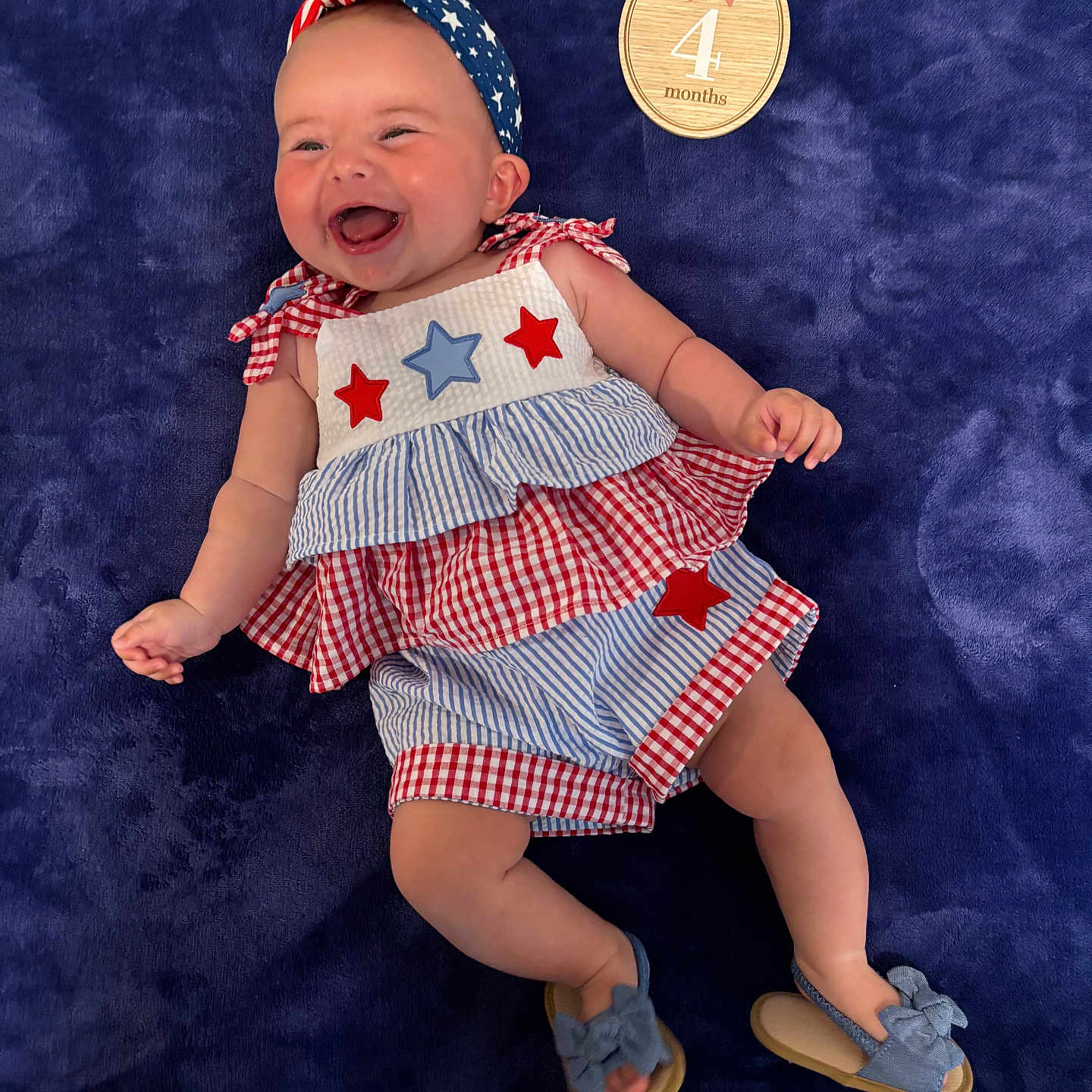 Sienna Rose joined the competition — help win amazing prizes! baby, infant, smiling, headband, dress, blue_blanket, wooden_plaque, milestone, happy, cute, footwear, sandals, red_white_blue, stars, stripes, lying_down, portrait, celebration, child, four_months