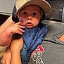 Lucas is registered to the contest to win money with this photo: baby, child, cap, hat, bib, hand, face, eyes, expression, person, adult, arm, clothing, shirt, kitchen, oven, indoor, surprised, holding, portrait