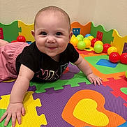 Aurora joined the competition — help win amazing prizes! baby, child, playmat, colorful, foam_puzzle, toy_balls, crawling, smiling, indoor, play_area, happy, cute, black_shirt, pink_shorts, soft_lighting, face, hands, floor_mat, puzzle_pieces, playpen