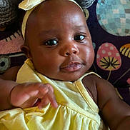 De'Vani is registered to the contest to win money with this photo: baby, child, yellow_dress, headband, bow, face, hand, infant, cute, portrait, closeup, dark_skin, expression, patterned_blanket, colorful_background, indoors, smile, young_child, soft_lighting, happy