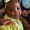 baby, child, yellow_dress, headband, bow, face, hand, infant, cute, portrait, closeup, dark_skin, expression, patterned_blanket, colorful_background, indoors, smile, young_child, soft_lighting, happy