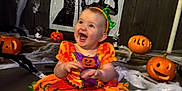 Dolcie-Rae is registered to the contest to win money with this photo: baby, carved_pumpkins, celebration, child, cobwebs, cute, decorations, festive, halloween, happy, headband, holiday, indoor, orange_dress, person, pumpkin_costume, shadow, sitting, smiling, wall