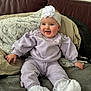 baby, blanket, child, comfortable, couch, cozy, cute, flower, happy, headband, indoors, infant, person, portrait, purple_clothing, sitting, smiling, soft_fabric, white_socks, young_child