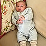 baby, infant, couch, pillow, onesie, socks, soft_fabric, floral_pattern, beige, light_blue, knitted, indoor, cute, child, portrait, relaxed, furniture, home, seated, small_hands