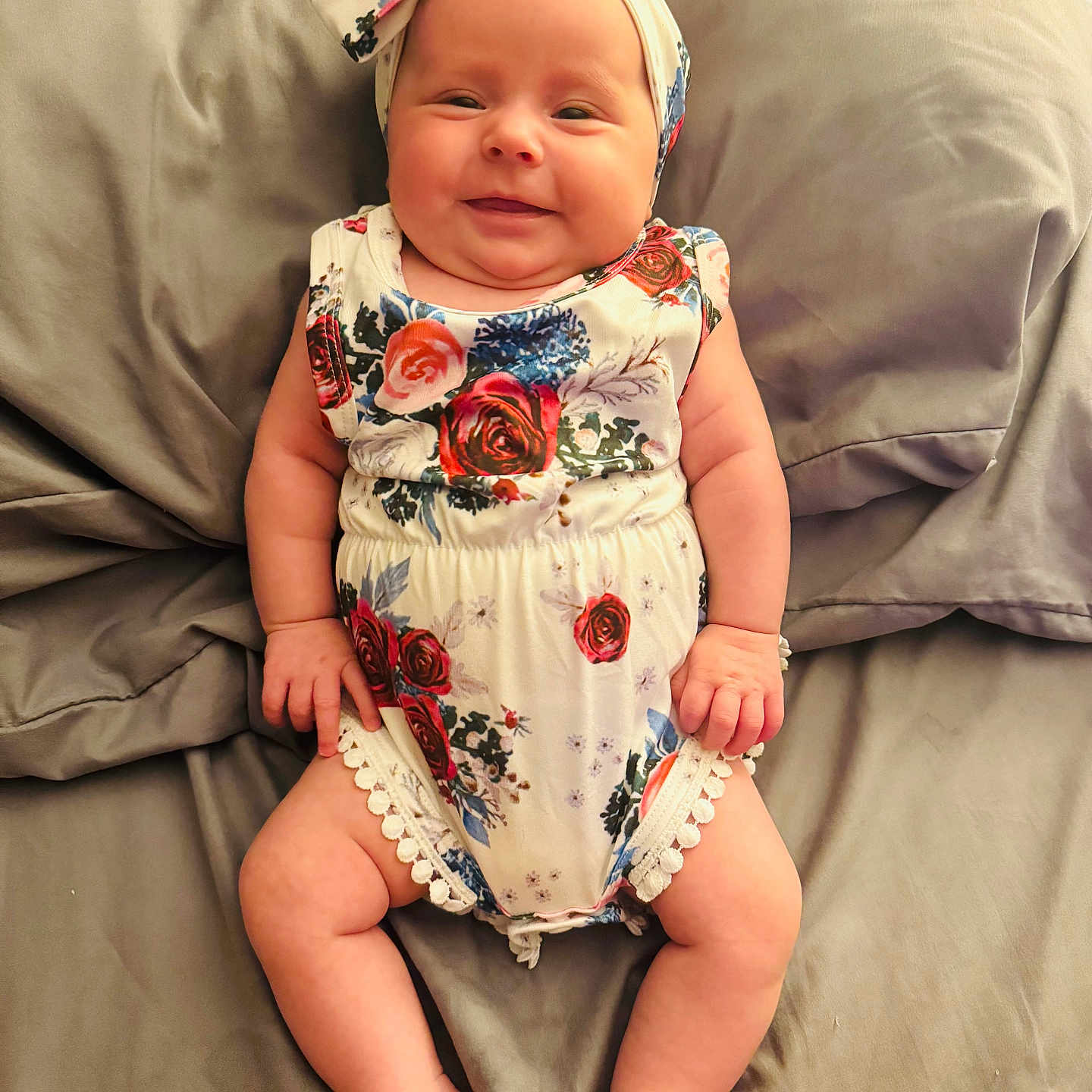 Brileigh is registered to the contest to win money with this photo: arms, baby, bed, child, comfort, cute, fabric, floral_pattern, happy, headband, indoors, infant, legs, lying_down, person, pillow, romper, skin, smile, soft
