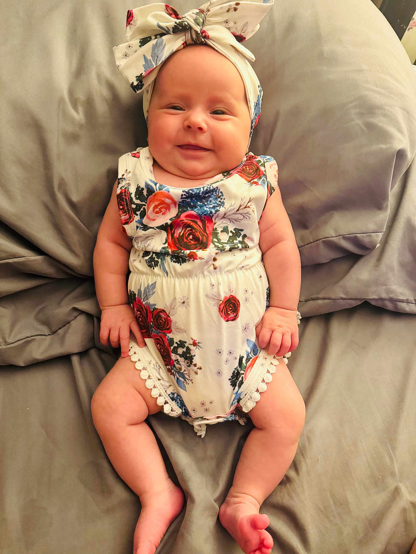 Brileigh is registered to the contest to win money with this photo: baby, infant, smile, headband, romper, floral_pattern, bed, pillow, skin, legs, arms, cute, happy, lying_down, child, indoors, fabric, soft, comfort, person