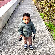 Kaïs a rejoint le concours — aidez-le/la à gagner de superbes lots ! child, toddler, puffer_jacket, mittens, sidewalk, urban, cars, bushes, fire_hydrant, curious, outdoor, street, winter_clothing, footwear, concrete, young_child, expression, standing, daylight, casual