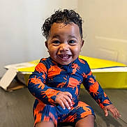 Zamari joined the competition — help win amazing prizes! baby, child, smiling, curly_hair, sitting, floor, blue_clothing, orange_crabs, happy, indoor, box, wooden_floor, cute, toddler, teeth, portrait, one_person, infant, playful, bright_colors