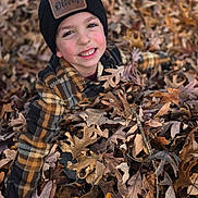 Oliver is registered to the contest to win money with this photo: child, boy, leaves, autumn, outdoor, smiling, hat, plaid_jacket, face, nature, play, fall, happy, seasonal, park, casual_clothing, person, fun, leaf_pile, cheerful