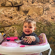 Catalena participe au concours pour gagner de l'argent avec cette photo : baby, child, clothing, cute, face, hand, happy, infant, outdoor, person, pink, playful, portrait, sitting, smiling, stone_wall, toy, walker, white, young