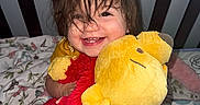 Airika joined the competition — help win amazing prizes! toddler, child, smiling, plush_toy, stuffed_animal, crib, bed, blanket, happy, cute, indoors, person, hair, face, hugging, red, yellow, soft_toy, infant, cozy