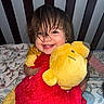 toddler, child, smiling, plush_toy, stuffed_animal, crib, bed, blanket, happy, cute, indoors, person, hair, face, hugging, red, yellow, soft_toy, infant, cozy