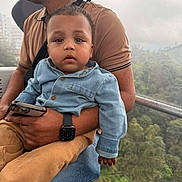 Yamin is registered to the contest to win money with this photo: adult, cable_car, casual_clothing, child, daytime, denim_jacket, forest, gondola, holding, nature, outdoor, person, sitting, smartphone, smartwatch, tan_pants, toddler, travel, trees, window