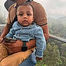 adult, cable_car, casual_clothing, child, daytime, denim_jacket, forest, gondola, holding, nature, outdoor, person, sitting, smartphone, smartwatch, tan_pants, toddler, travel, trees, window