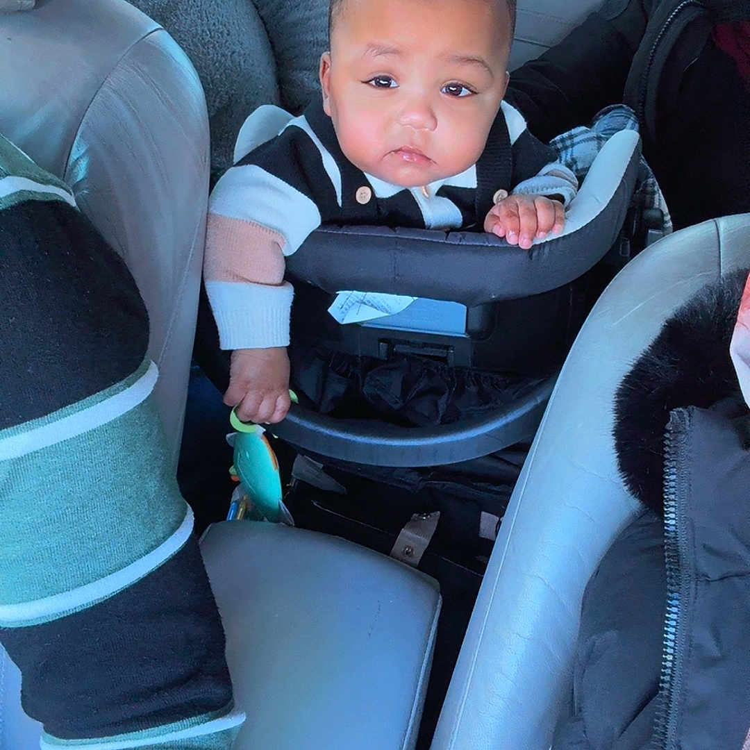 Yamin is registered to the contest to win money with this photo: adult, baby, car_interior, car_seat, child, clothing, face, hand, head, jacket, leather_seat, person, road, seat, seatbelt, toy, travel, vehicle, window, winter_wear