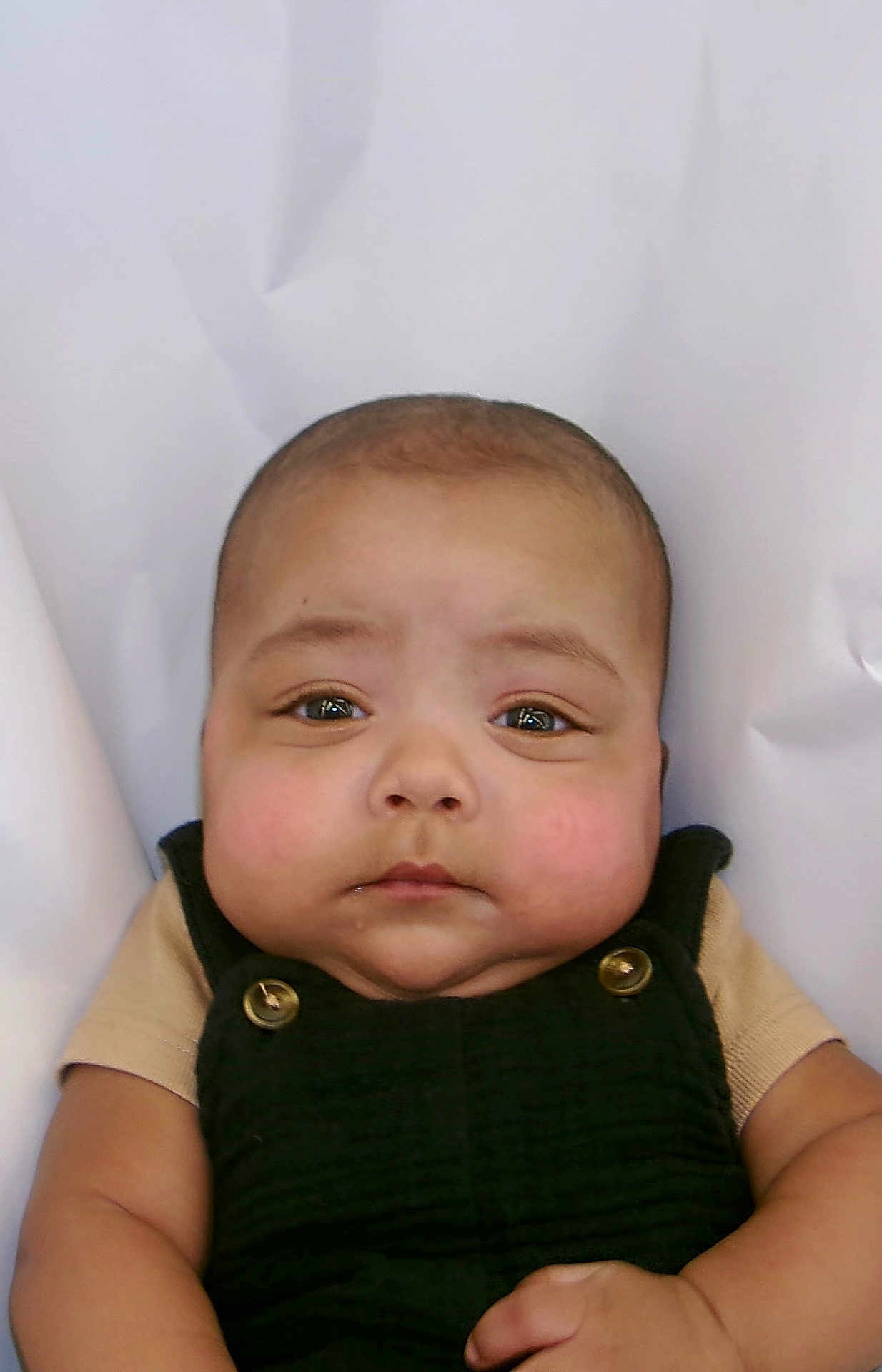 Yamin is registered to the contest to win money with this photo: baby, infant, face, eyes, cheeks, hands, clothing, overall, black, skin, portrait, expression, cute, child, young, background, white, soft, button, serious