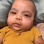 Yamin is registered to the contest to win money with this photo: baby, infant, child, face, cheeks, onesie, yellow_clothing, lightning_pattern, skin, hands, lying_down, bed, pillow, curious_expression, closeup, portrait, indoors, soft_texture, casual, cute