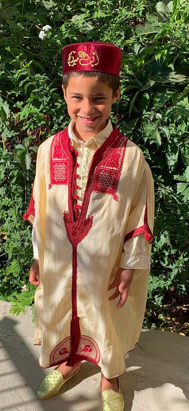 Mohammed participe au concours pour gagner de l'argent avec cette photo : academic_dress, button, costume, costume_hat, event, fashion_accessory, fashion_design, formal_wear, grass, hat, joy, mortarboard, pattern, peach, person, plant, red, sleeve, smile, toddler