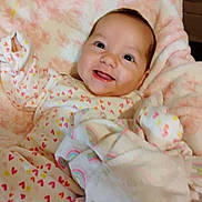 Ava is registered to the contest to win money with this photo: baby, smiling, infant, blanket, heart_pattern, onesie, cute, soft, cozy, child, portrait, happy, indoors, warm, comfort, person, face, pink, fabric, sleepwear