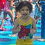 Arianelys Otero is registered to the contest to win money with this photo: child, girl, swimsuit, yellow_shorts, water_splash, water_park, playing, happy, curly_hair, summer, outdoor, kids, fun, clapping, splash_pad, colorful, smiling, people, water_drops, active