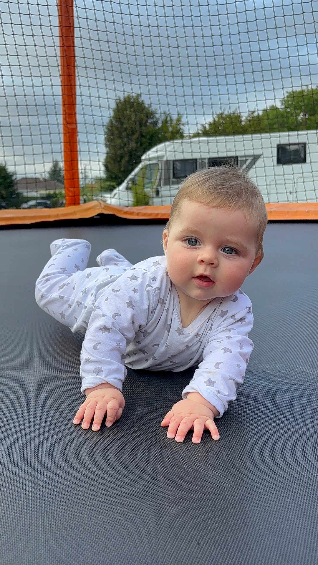 Alessio participe au concours pour gagner de l'argent avec cette photo : baby, child, pajamas, crawling, trampoline, outdoor, grass, netting, face, hands, blue_eyes, curious, expression, vehicle, camper_van, sky, trees, daytime, play, infant