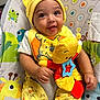 baby, child, smiling, yellow_clothing, hat, bib, plush_toy, baby_seat, patterned_fabric, giraffe, frog, toddler, cute, happy, indoors, soft_toy, infant, colorful, playful, comfort