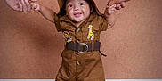Zenith is registered to the contest to win money with this photo: toddler, child, smiling, brown_outfit, hat, standing, holding_hands, wooden_floor, indoor, cute, happy, animal_patches, belt, barefoot, two_hands, portrait, warm_background, playful, people, family