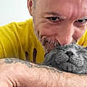 Smokey is registered to the contest to win money with this photo: man, cat, gray_cat, pet, cuddle, affection, portrait, close_up, yellow_shirt, tattoo, arm, face, paw, relaxed, indoor, human, animal, happy, love, furry