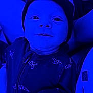 Reign is registered to the contest to win money with this photo: baby, infant, newborn, face, hat, onesie, zipper, smile, eyes, hand, arm, portrait, closeup, indoor, blue_lighting, fabric, pattern, holding, parent, cozy