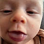 baby, infant, close_up, face, tongue_out, sticking_tongue, nose, eyes, bald_head, mouth, lips, skin, cheek, onesie, clothing, brown_clothing, blurred, out_of_focus, portrait, indoor