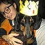 boy, child, dog, dachshund, glasses, crown, indoor, smile, pet, hand, food, croissant, clothing, portrait, face, cute, animal, brown, black, happy
