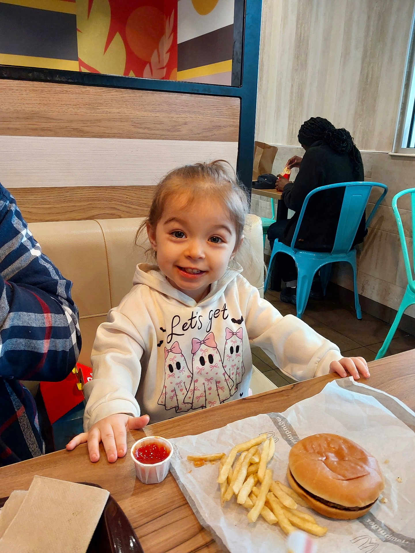 Chloe joined the competition — help win amazing prizes! child, smile, hoodie, food, burger, french_fries, ketchup, table, restaurant, person, chair, indoor, casual_clothing, happy, face, hair, wood, napkin, seat, fast_food