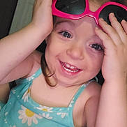 Chloe is registered to the contest to win money with this photo: toddler, child, smile, dress, sunglasses, pink, blue, daisy, flower_pattern, happy, indoor, playful, face, person, cute, hand, young_child, portrait, clothing, skin