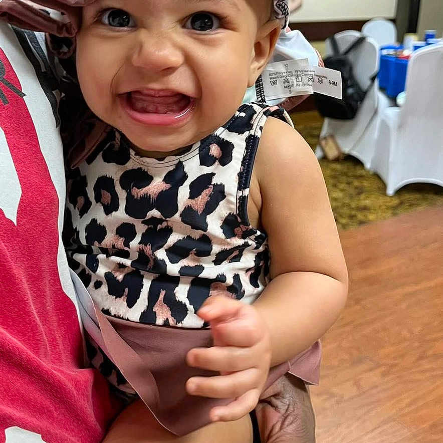 Jazzylnn joined the competition — help win amazing prizes! baby, child, smiling, leopard_print, hat, clothing, person, indoor, holding, hand, face, happy, cute, infant, portrait, fashion, people, wood_floor, table, chair