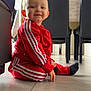 toddler, child, red_tracksuit, sitting, floor, smiling, indoor, tiles, black_chairs, table, casual, home, young_child, portrait, clothing, person, cute, happy, baby, light