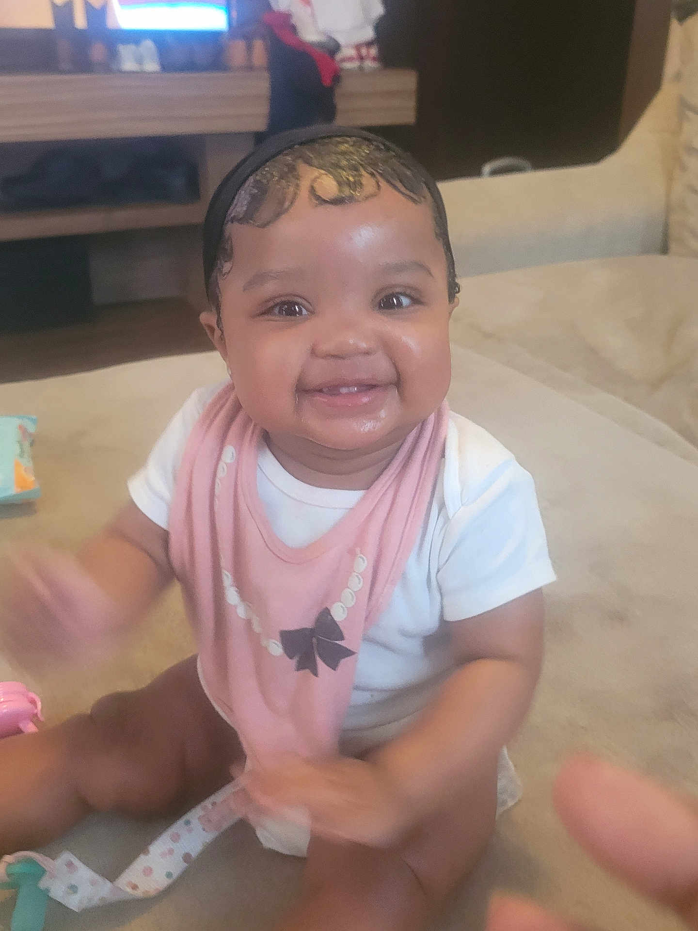 Zuri is registered to the contest to win money with this photo: baby, infant, smiling, bib, sitting, indoor, couch, toy, headband, drool, chubby_cheeks, eyes, teeth, hand_motion, portrait, cute, family_room, soft_lighting, skin, happy