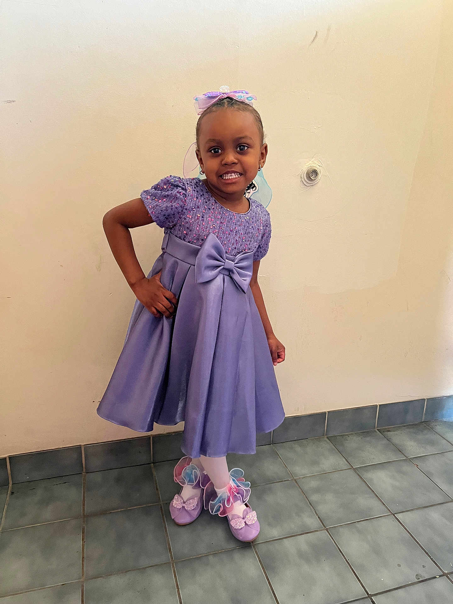 Anaiyiah is registered to the contest to win money with this photo: child, girl, purple_dress, bow, headband, smile, pose, shoes, ribbons, tights, earrings, indoor, tile_floor, wall, happy, fashion, portrait, cute, person, standing