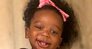 Love is registered to the contest to win money with this photo: baby, baby_girl, black_clothing, cheerful, child, closeup, curly_hair, cute, face, happy, headshot, indoors, infant, person, pink_bow, portrait, skin, smiling, toddler, young_child