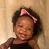 baby, smiling, child, curly_hair, pink_bow, black_clothing, portrait, cute, happy, infant, face, person, indoors, young_child, headshot, closeup, baby_girl, skin, cheerful, toddler