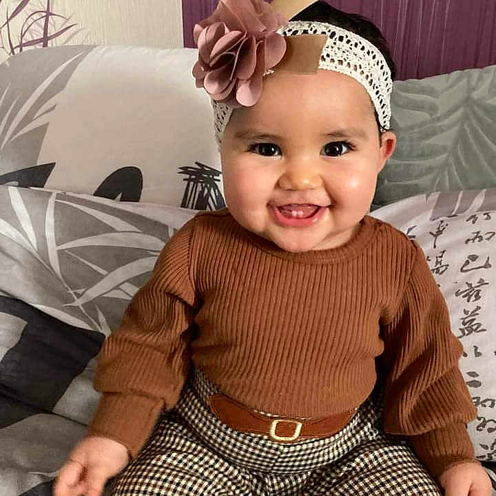 Leïlla a rejoint le concours — aidez-le/la à gagner de superbes lots ! accessories, baby, babylaughing, clothing, couch, cushion, face, furniture, happy, head, headband, homedecor, knitwear, pants, person, photography, portrait, sitting, smile, sweater